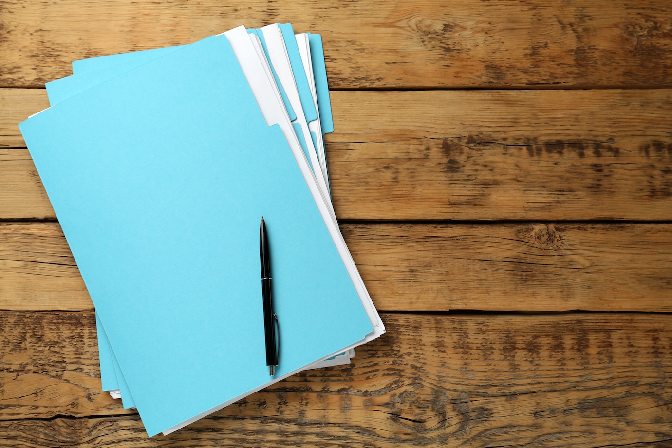 Turquoise files with documents and pen on wooden table, top view