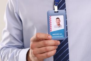 Medical assistant with badge on light background, closeup